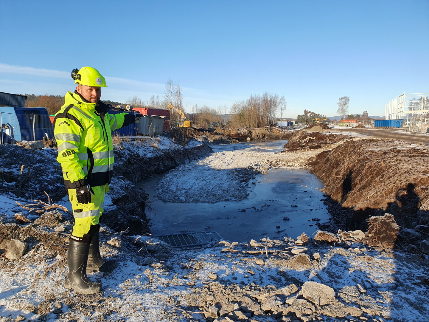 Byggeleder Lars Willy Moland i Vestfold og Telemark fylkeskommune ved den første rundkjøringen som graves nå, foreløpig som et hull i bakken. Rundkjøringen nummer to blir på fylkesvegen, ved siden av det det nye bygget til Tesla (stillas til høyre). (Foto: Bypakke Grenland)